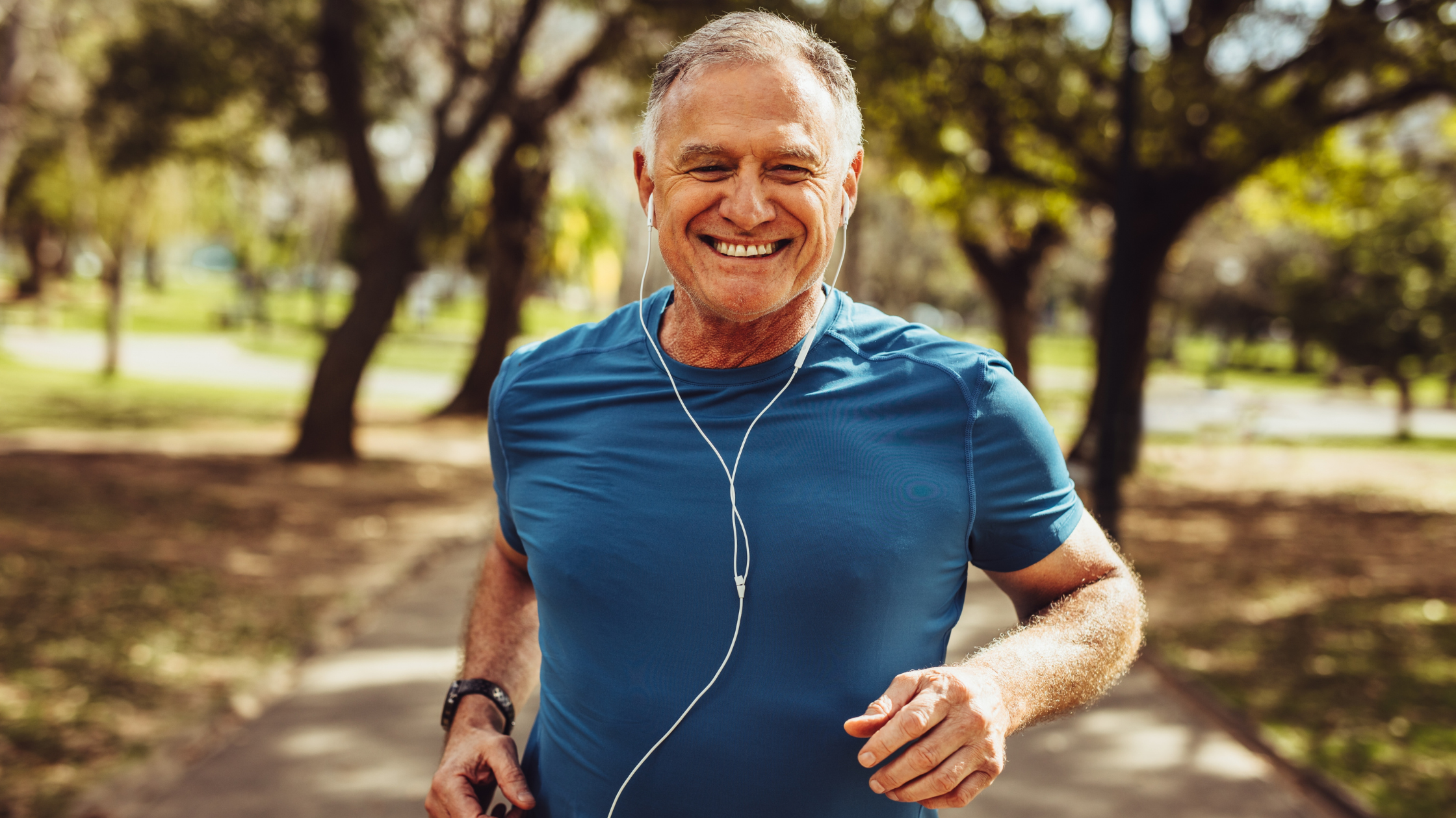 senior man smiles while running through a park