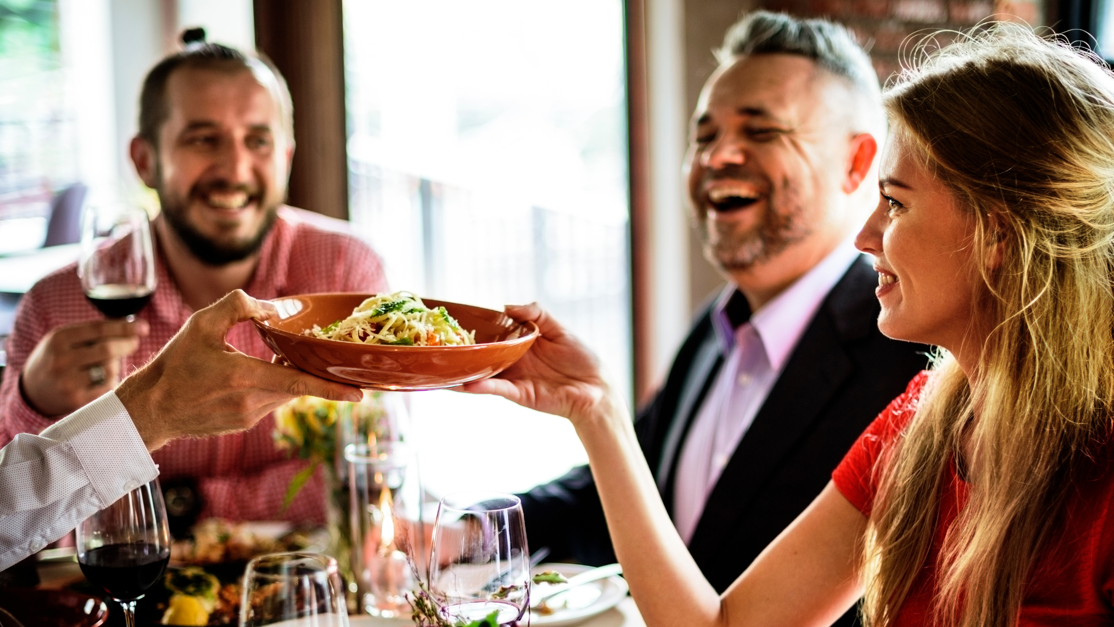 Laughing group of people enjoy their meal fresh salads and enjoy some red wine