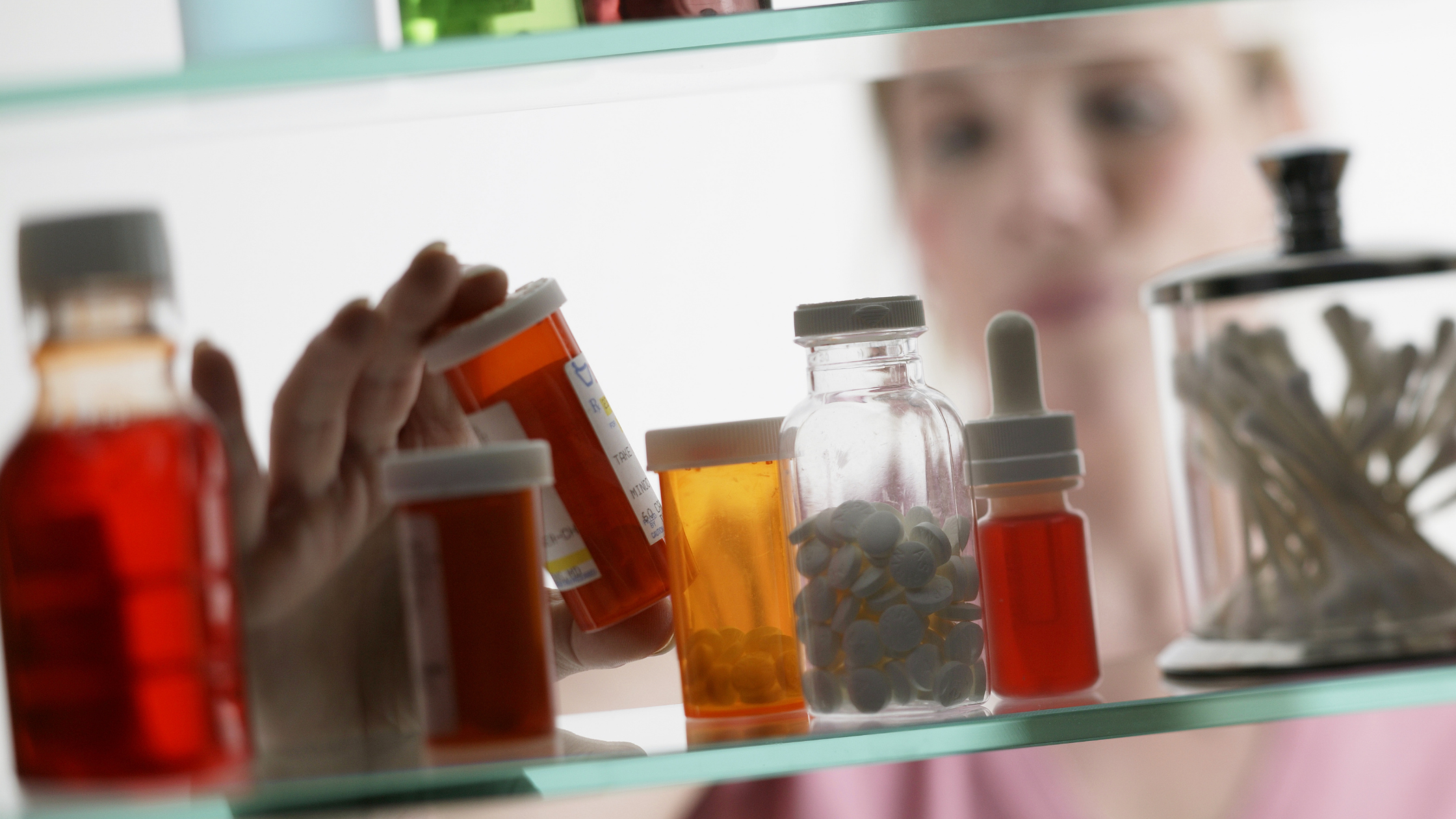 Woman considers medication bottle pulled from cabinet with many other medication bottles