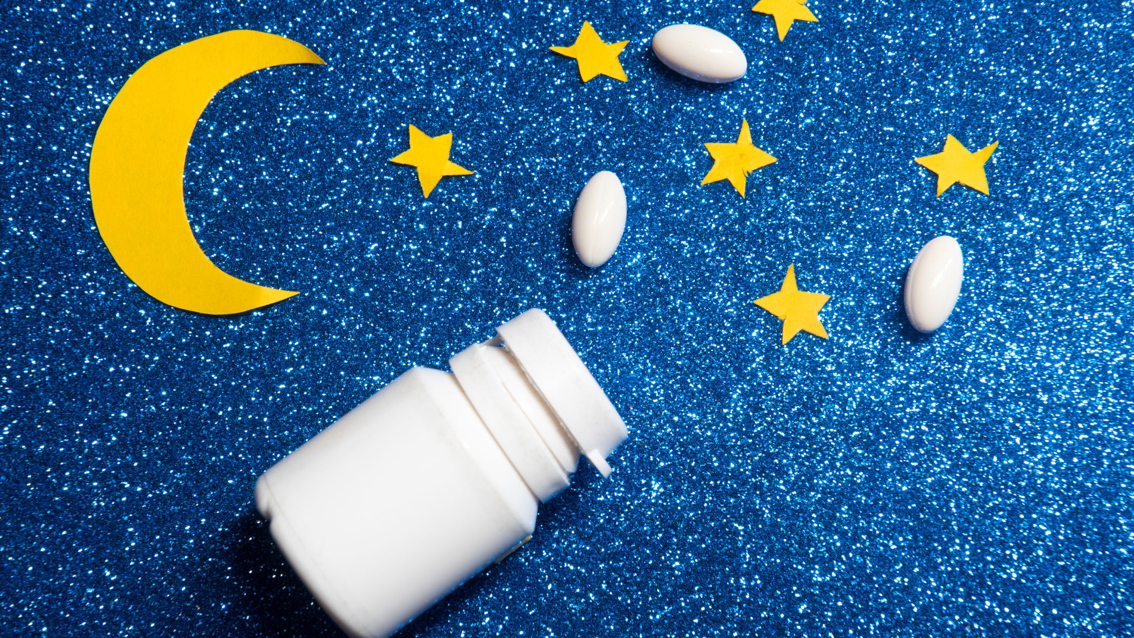 white pill bottle open on sparkly blue background with moon and stars