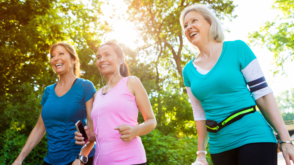 three senior women smile while walking together outdoors