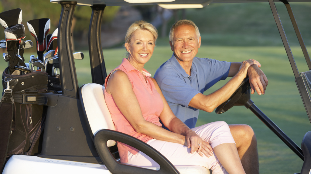 smiling seniors drive a golf cart across a course