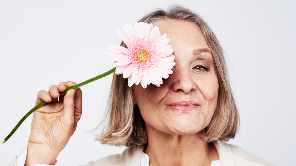 senior woman holds a flower up in front of her eye