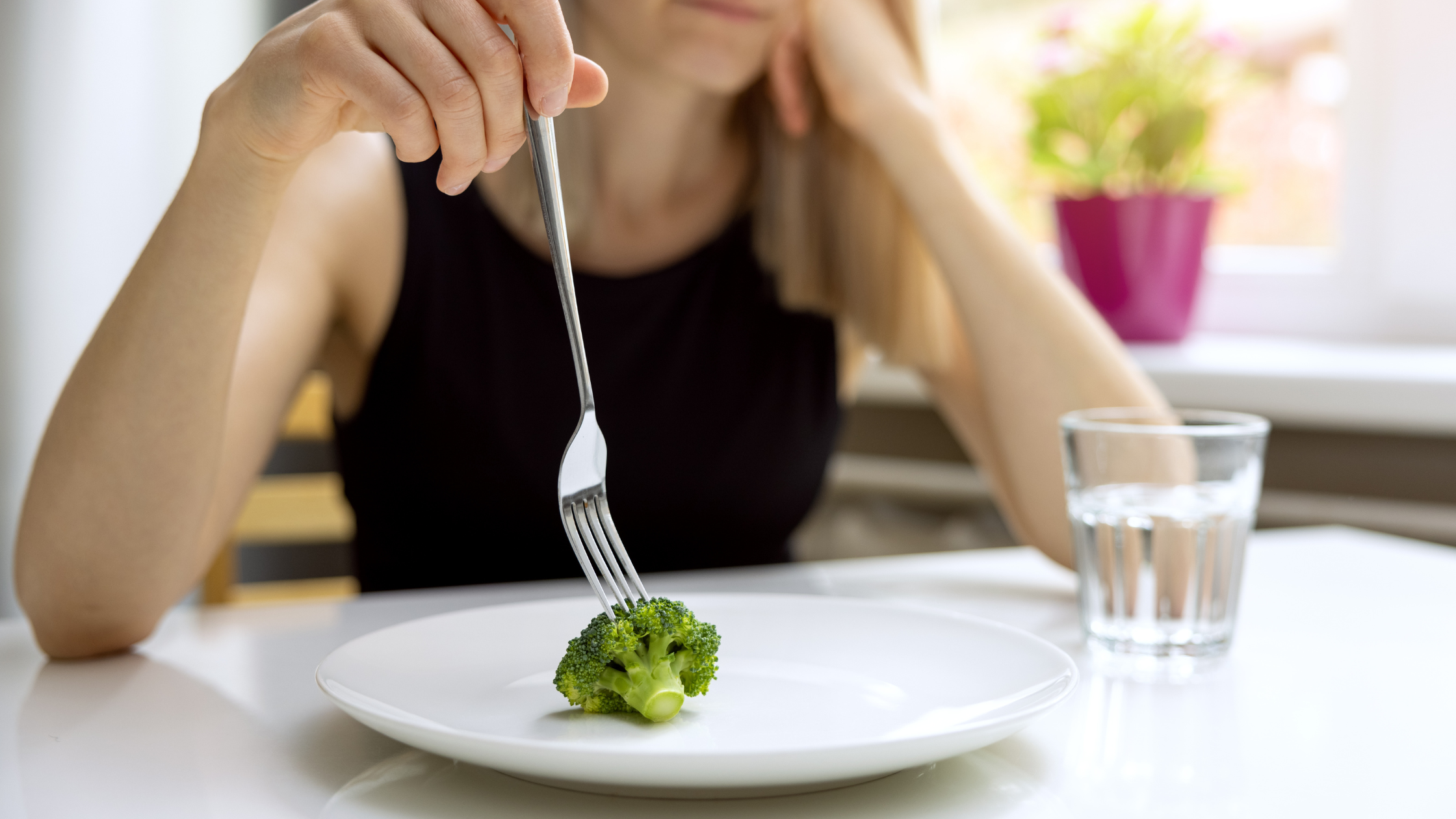 woman plays with a single piece of broccoli on a dinner plate