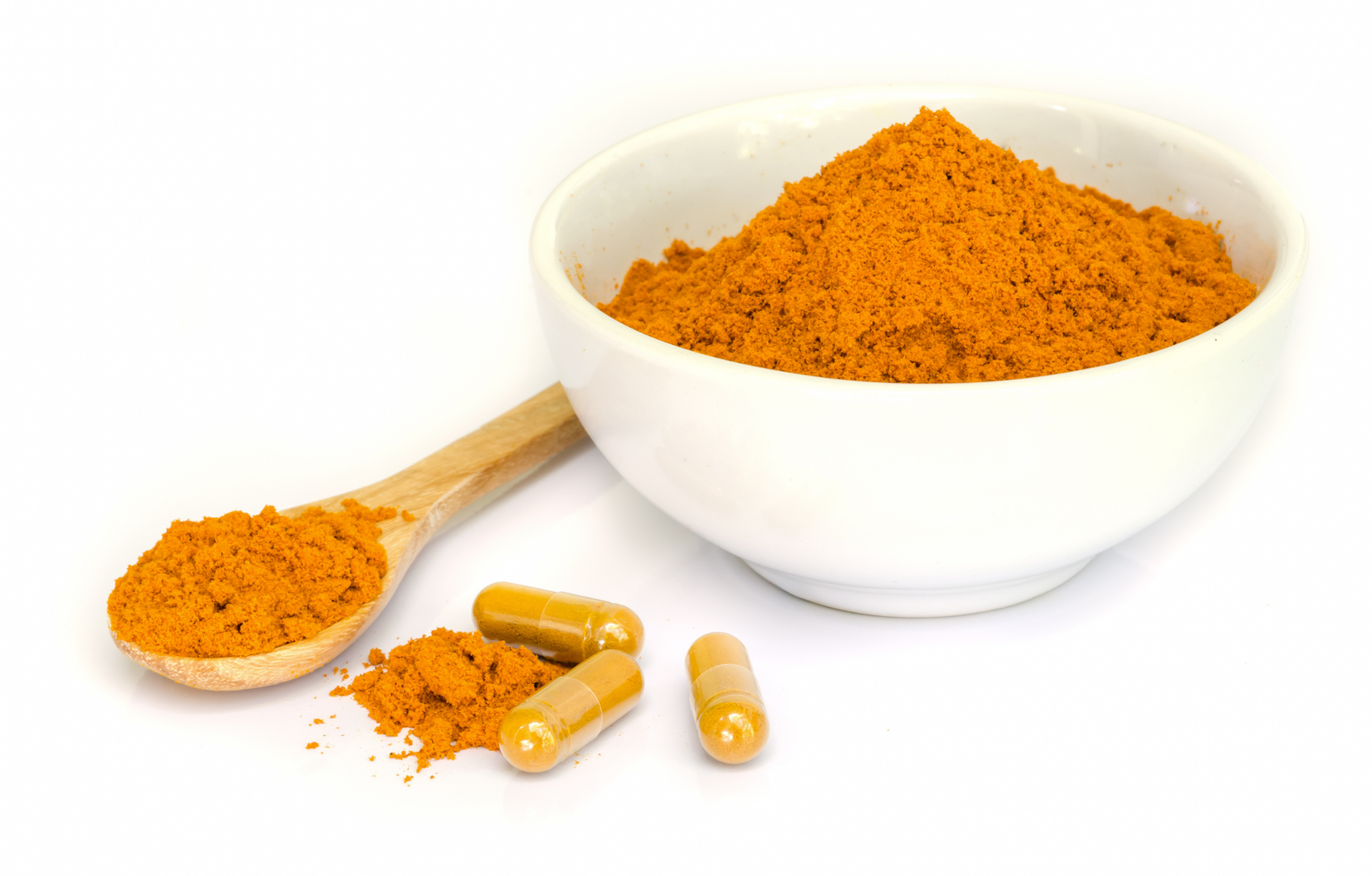 Small bowl full of orange powder, a wooden spoon and pill capsules  with the same powder lying next to the bowl