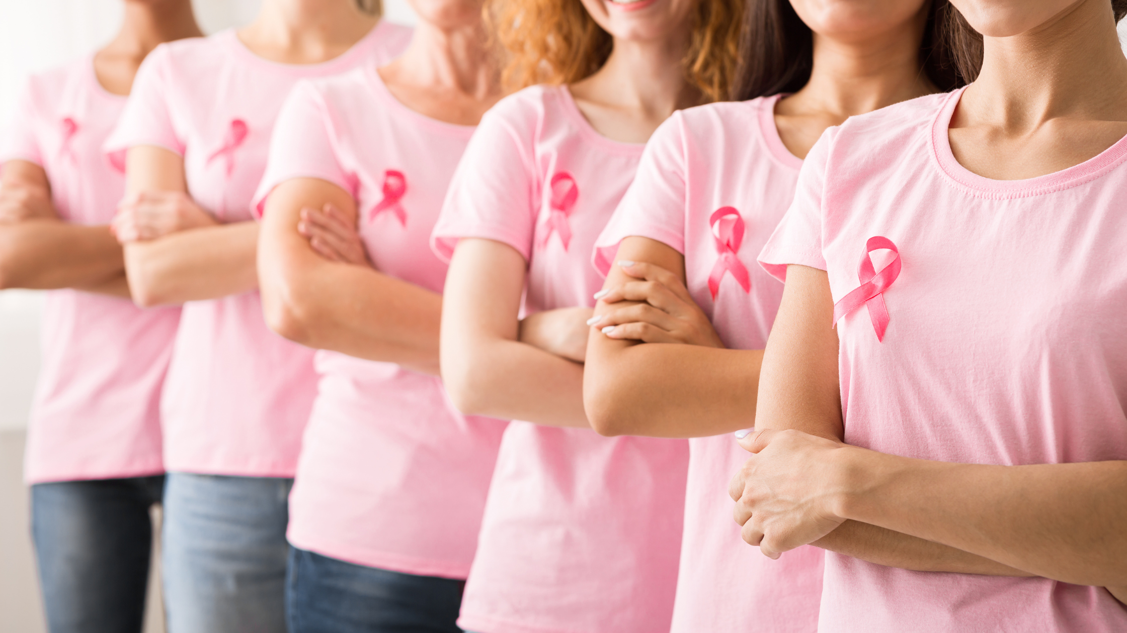 row of women stand with pink cancer ribbons on their shirts