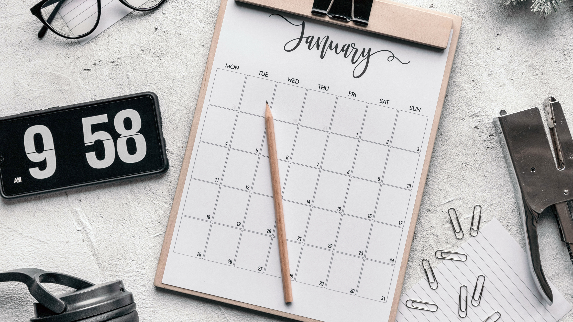 table with a notepad, calendar of January, paperclips, and glasses