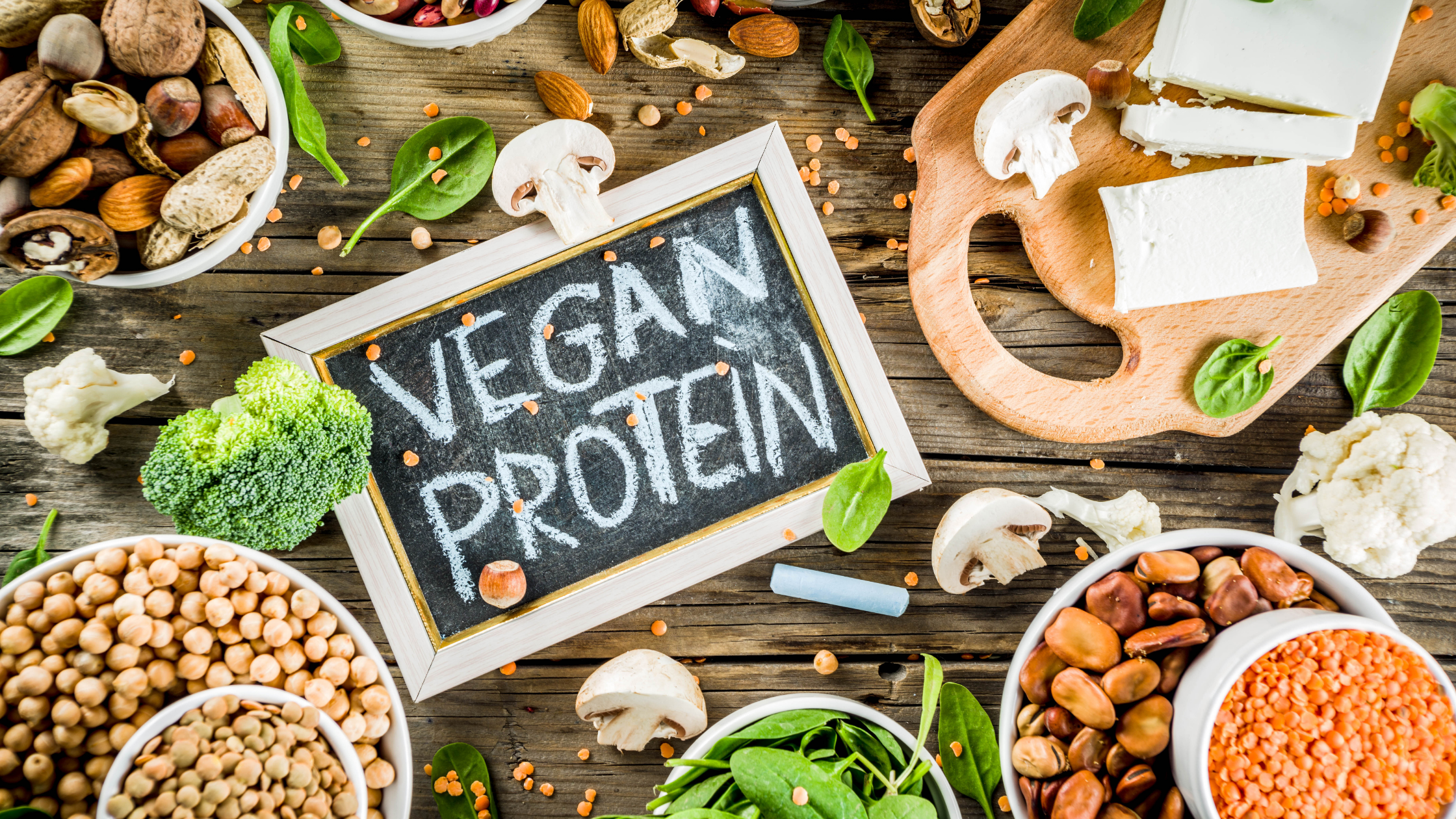 Blackboard with the words "Vegan Protein" surrounded by nuts, mushrooms, vegetables, and other vegan foods