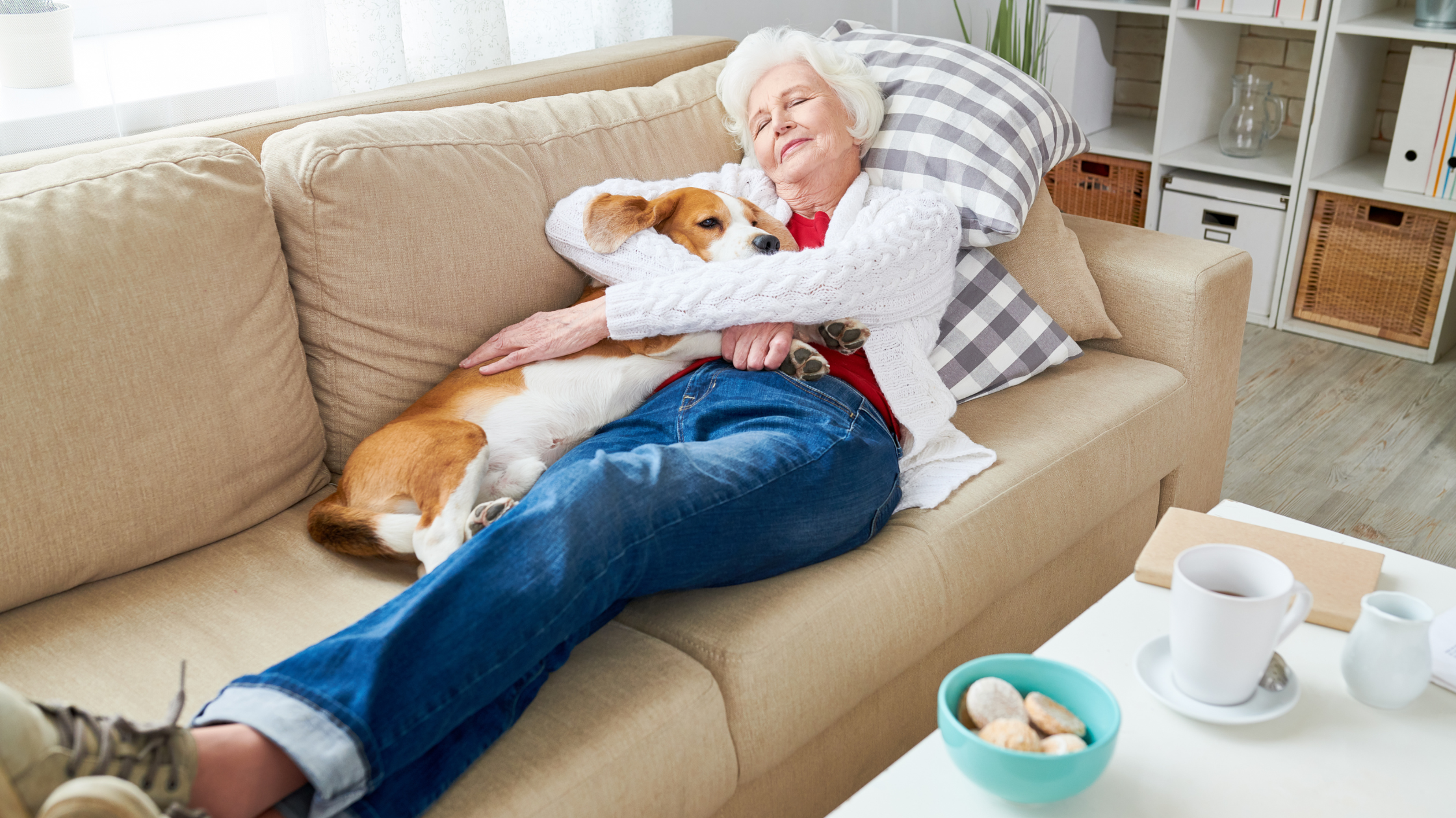 senior woman sleeps on a couch snuggling a dog