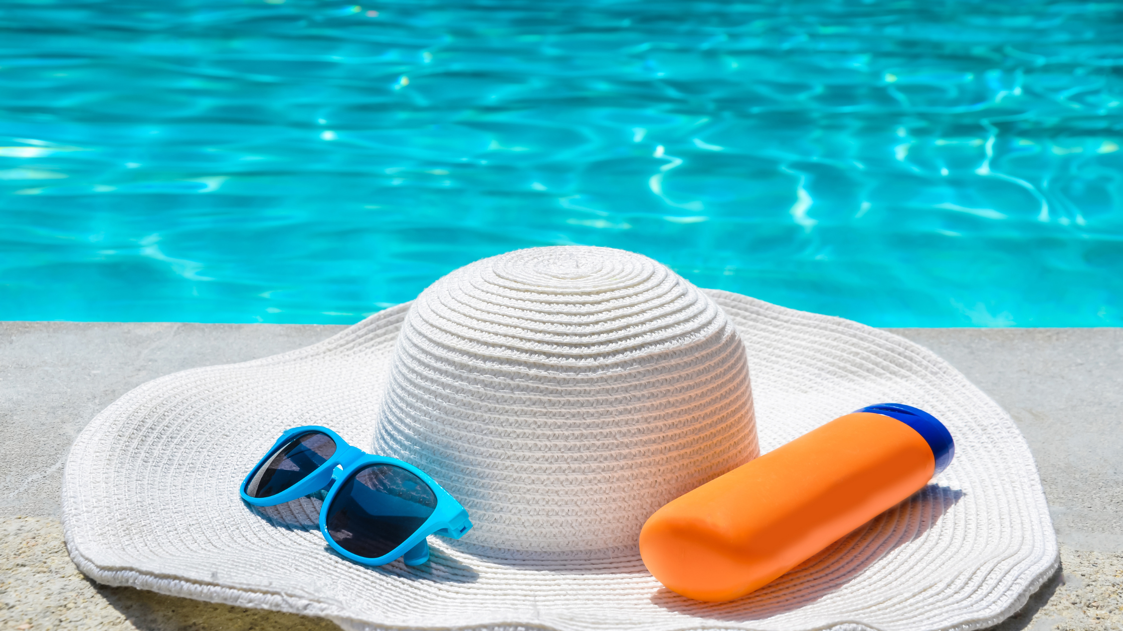 hat sitting by the pool with sunscreen and sunglasses