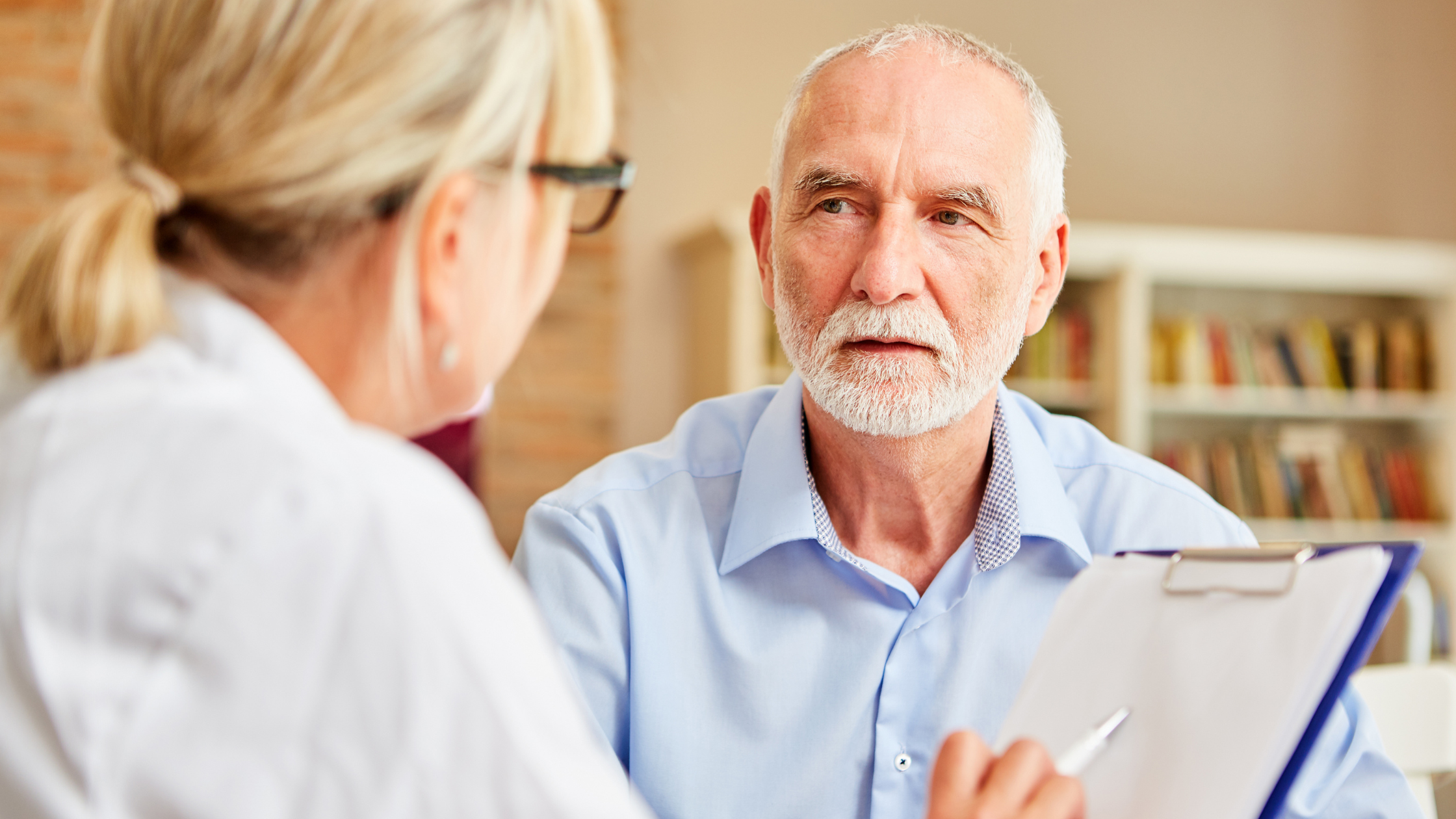 doctor holding a clipboard talks to a senior man