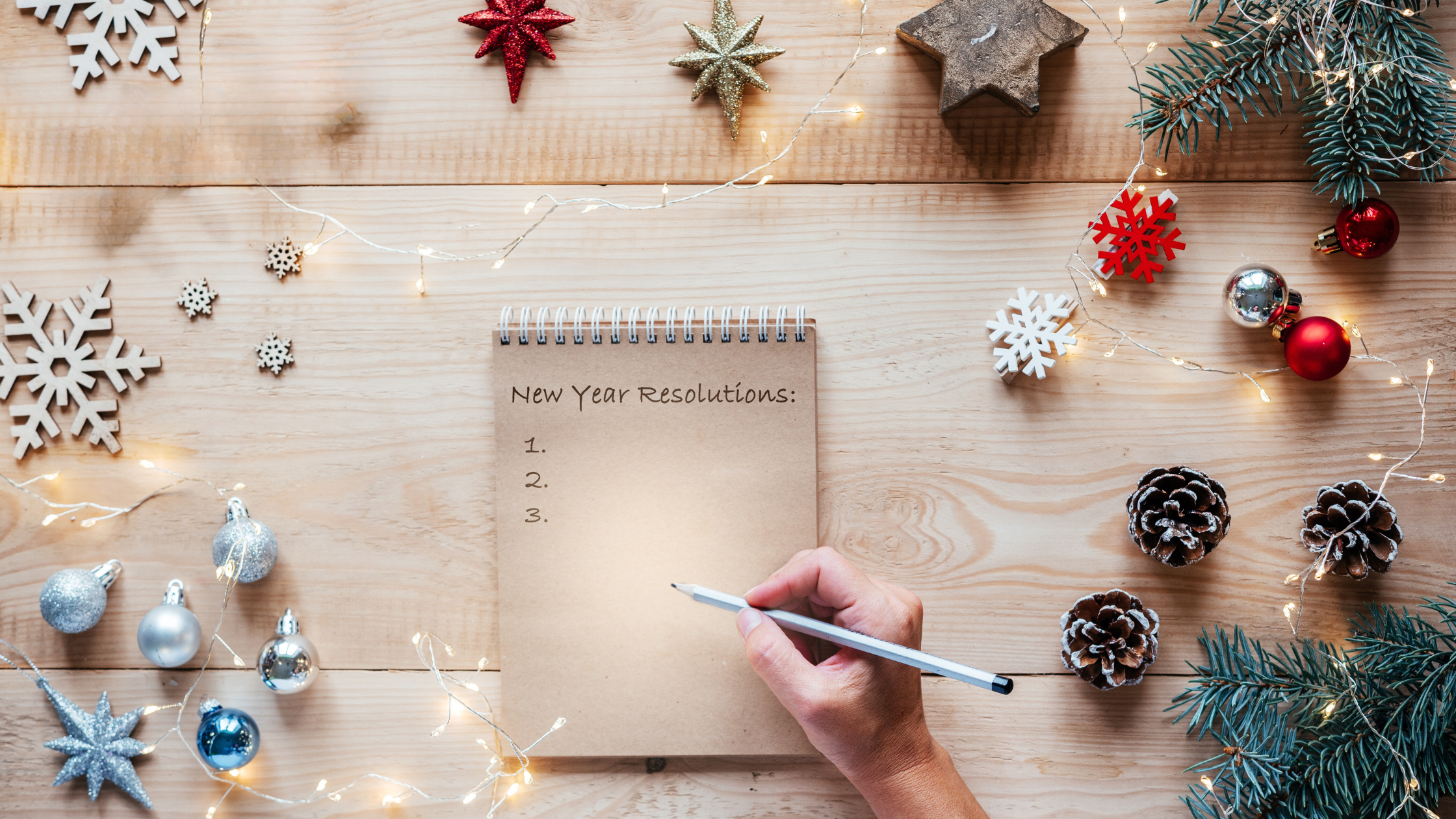 hand holds a pen over a notebook reading "new year's resolutions" and a black list