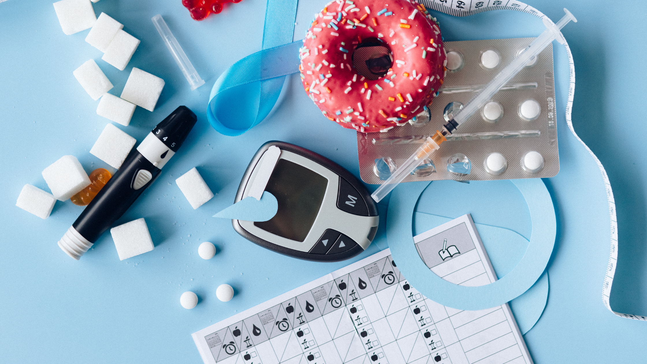 tabletop covered in needles, diabetes tests, donuts, and medicine