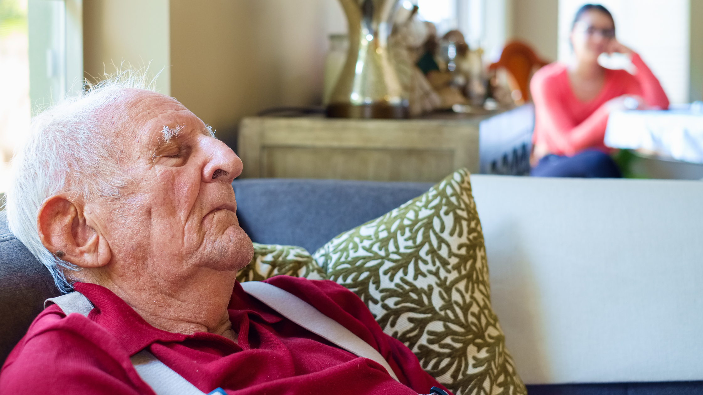 senior sleeps on the couch while family visits in the next room