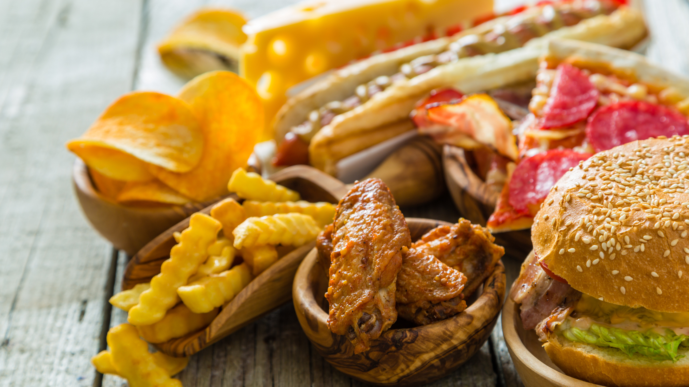 table covered in fatty foods like burgers, fries, and pizza