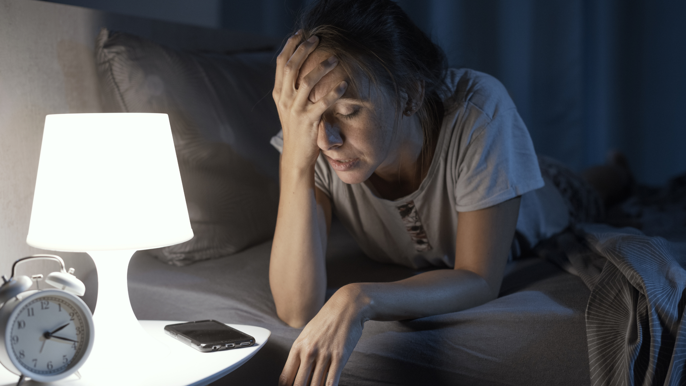 woman sits with head on her hands in a dark bedroom