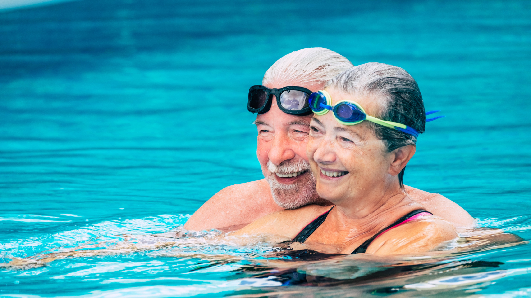 smiling senior couple float in a pool