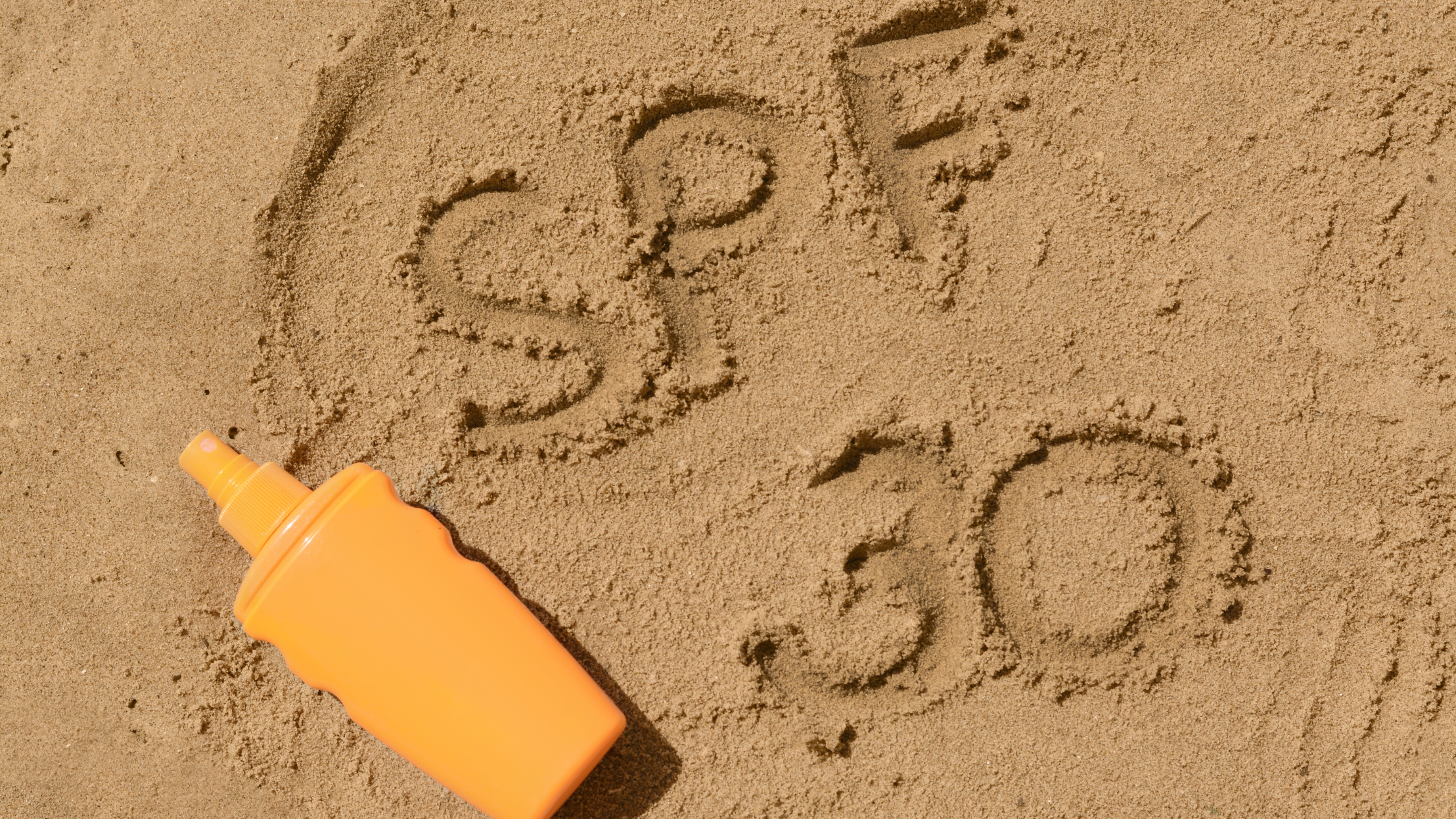 bottle of sunscreen laying on the sand with "spf 30" written beside it