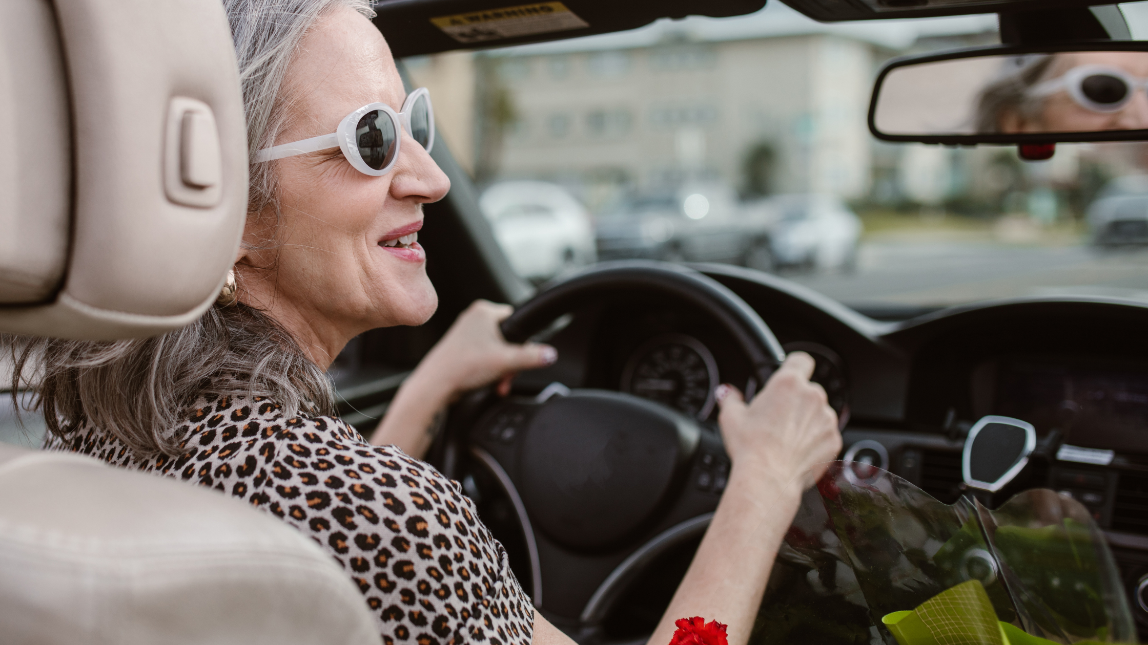 senior woman in sunglasses drives a car