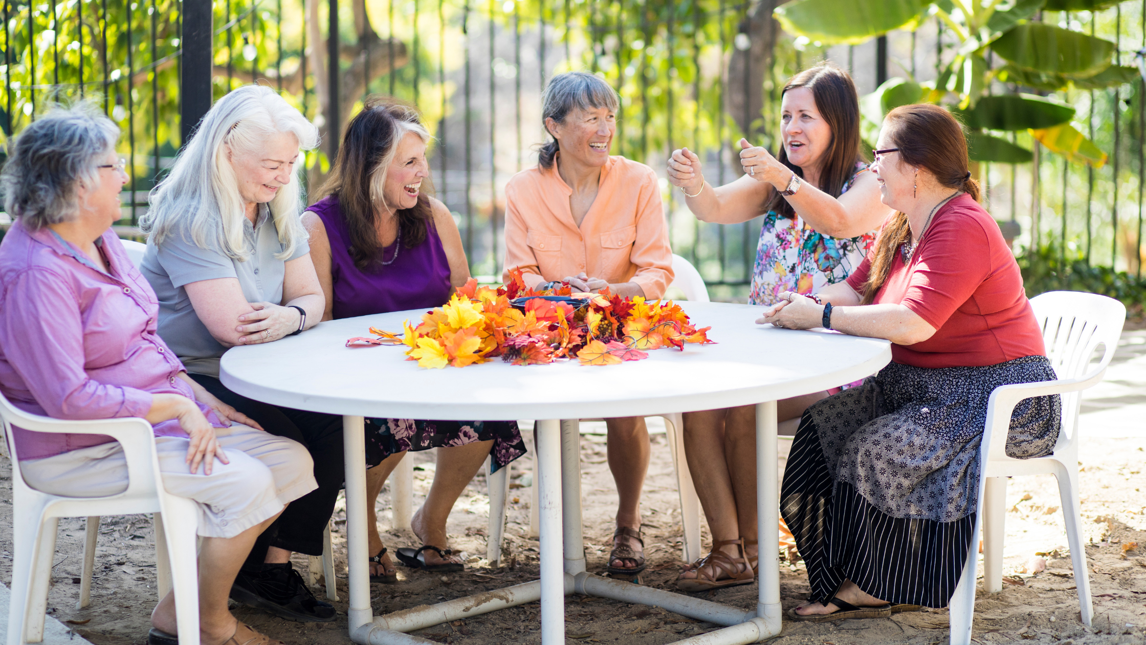 group of six senior women sitting around a table chatting joyfully