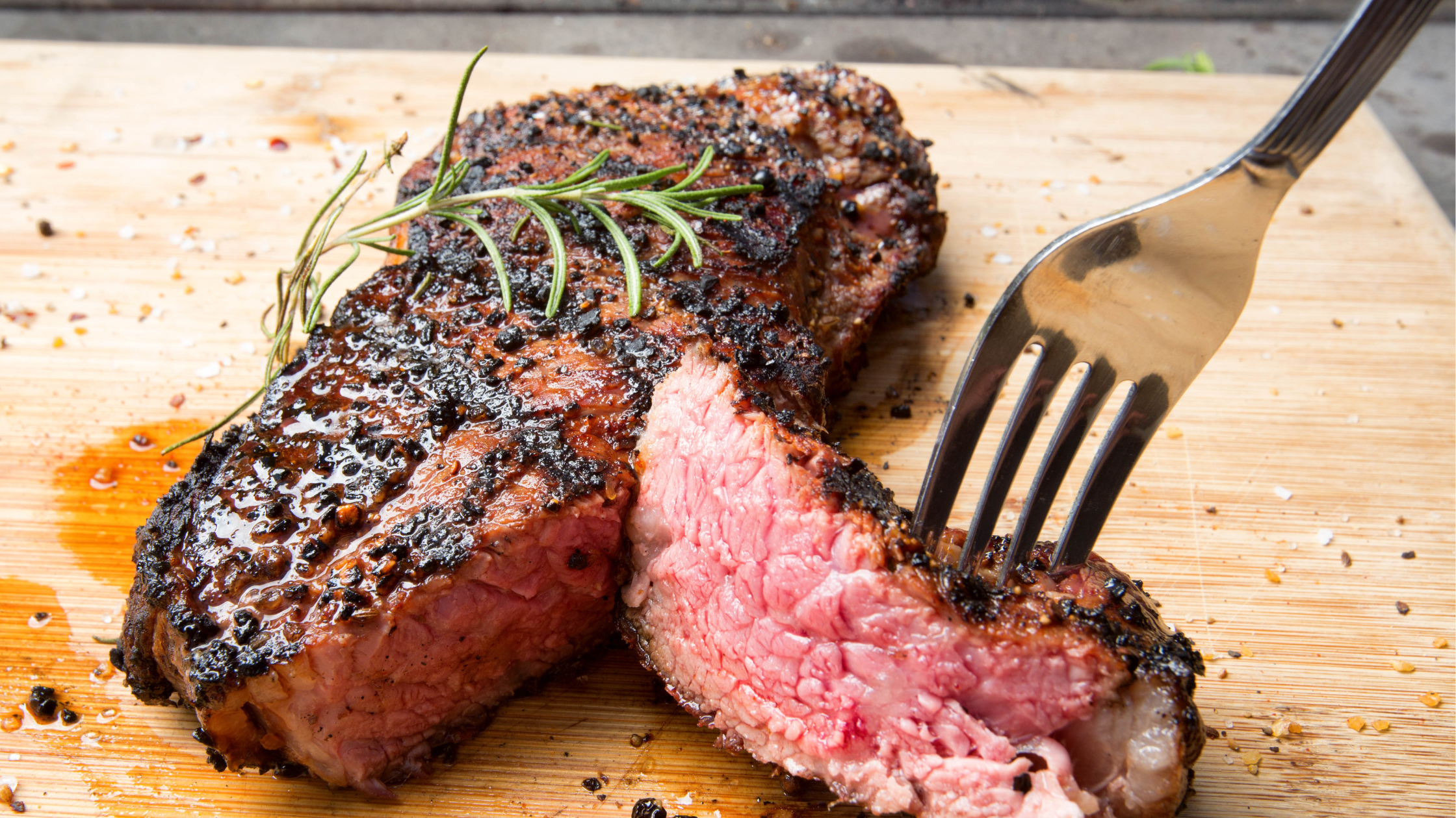 fork pulls a slice of medium-rare steak apart on a wooden cutting board