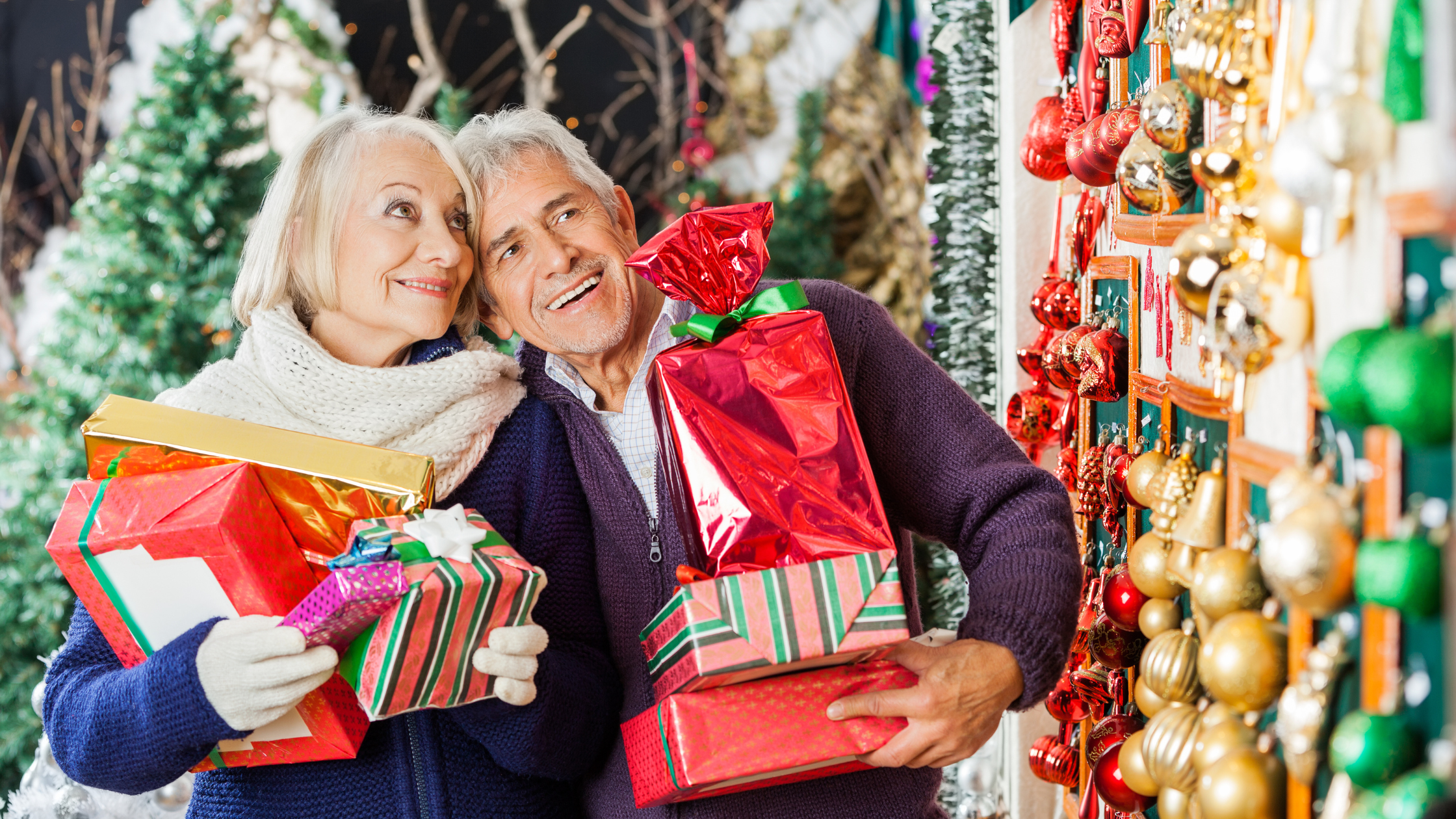 senior couple with arms full of gifts look at ornaments