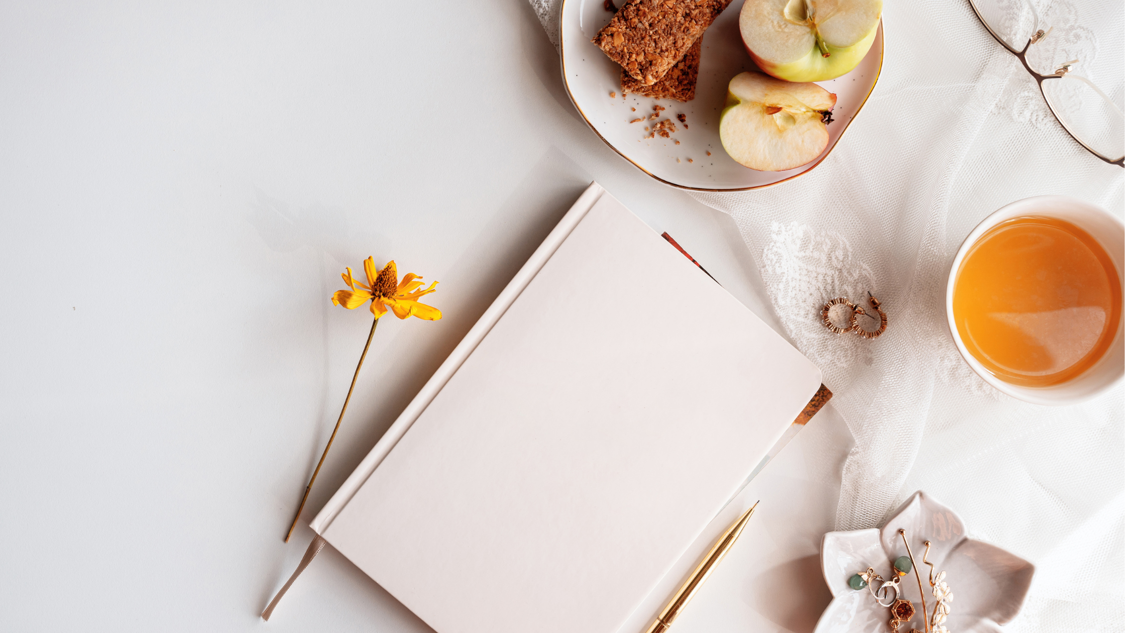 artfully arranged tabletop with tea, a notebook, healthy snacks, and some jewelry