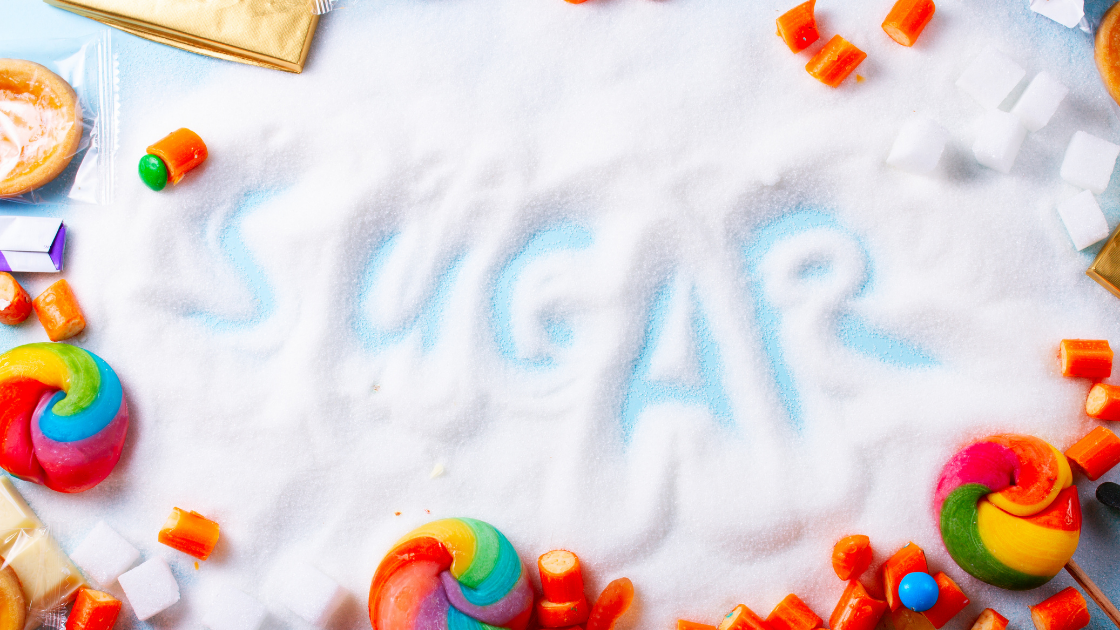 The word "Sugar" written in a pile of sugar, surrounded by candy