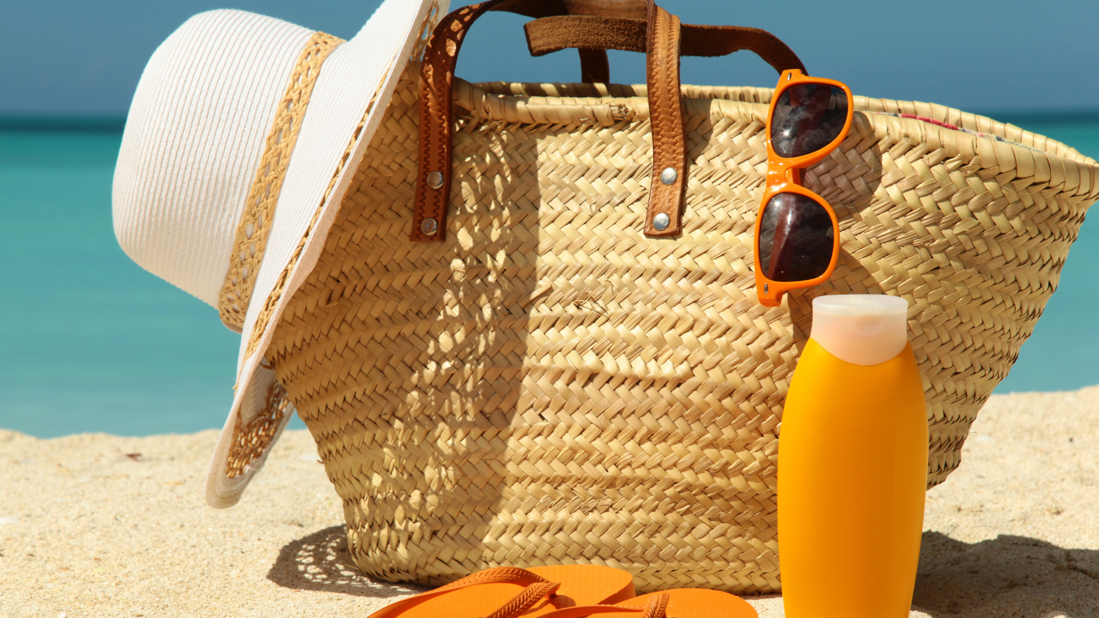 bag with a hat and sunglasses sitting next to a bottle of sunscreen
