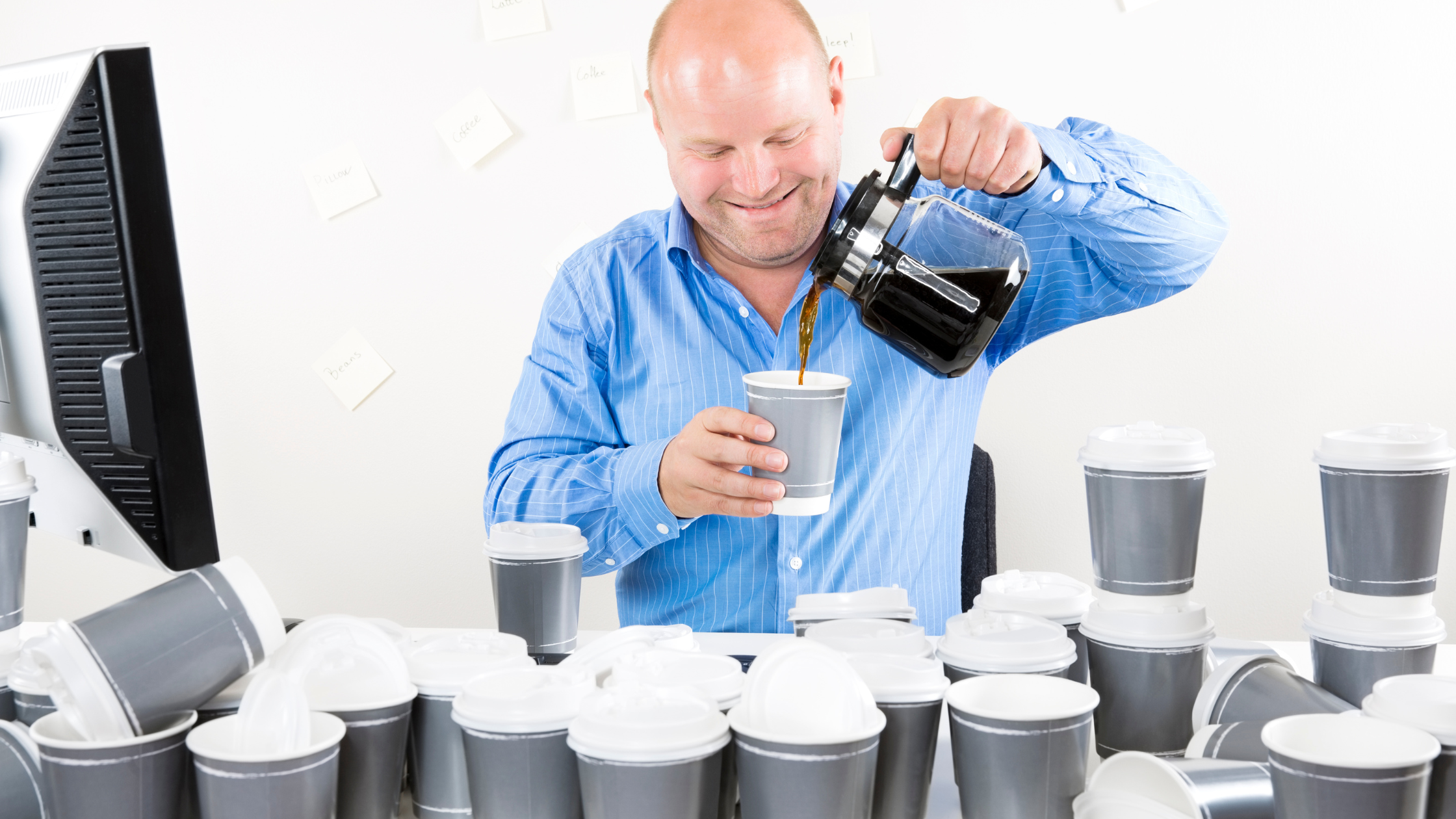 office worker surrounded by empty cups smiles manically as he pours himself more coffee 