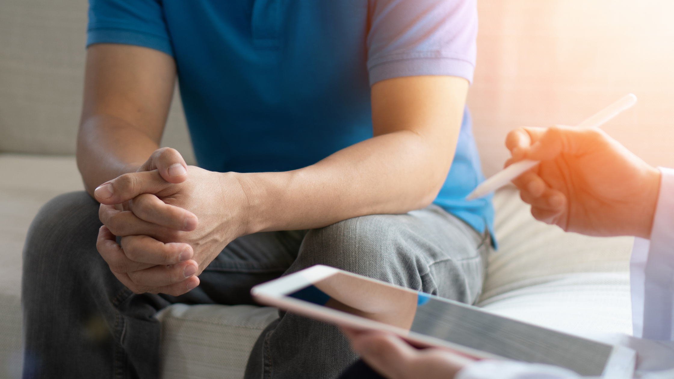 Man with clasped hands listens to doctor who has a tablet in hand