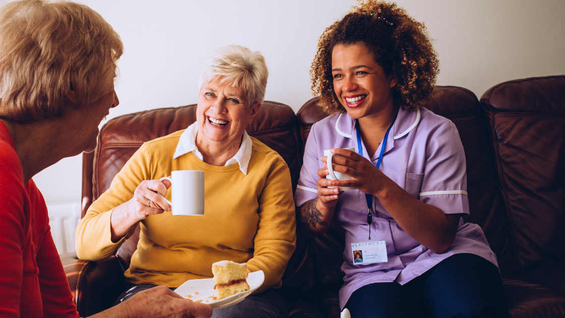 Two older women and a nurse happily enjoy coffee and tea