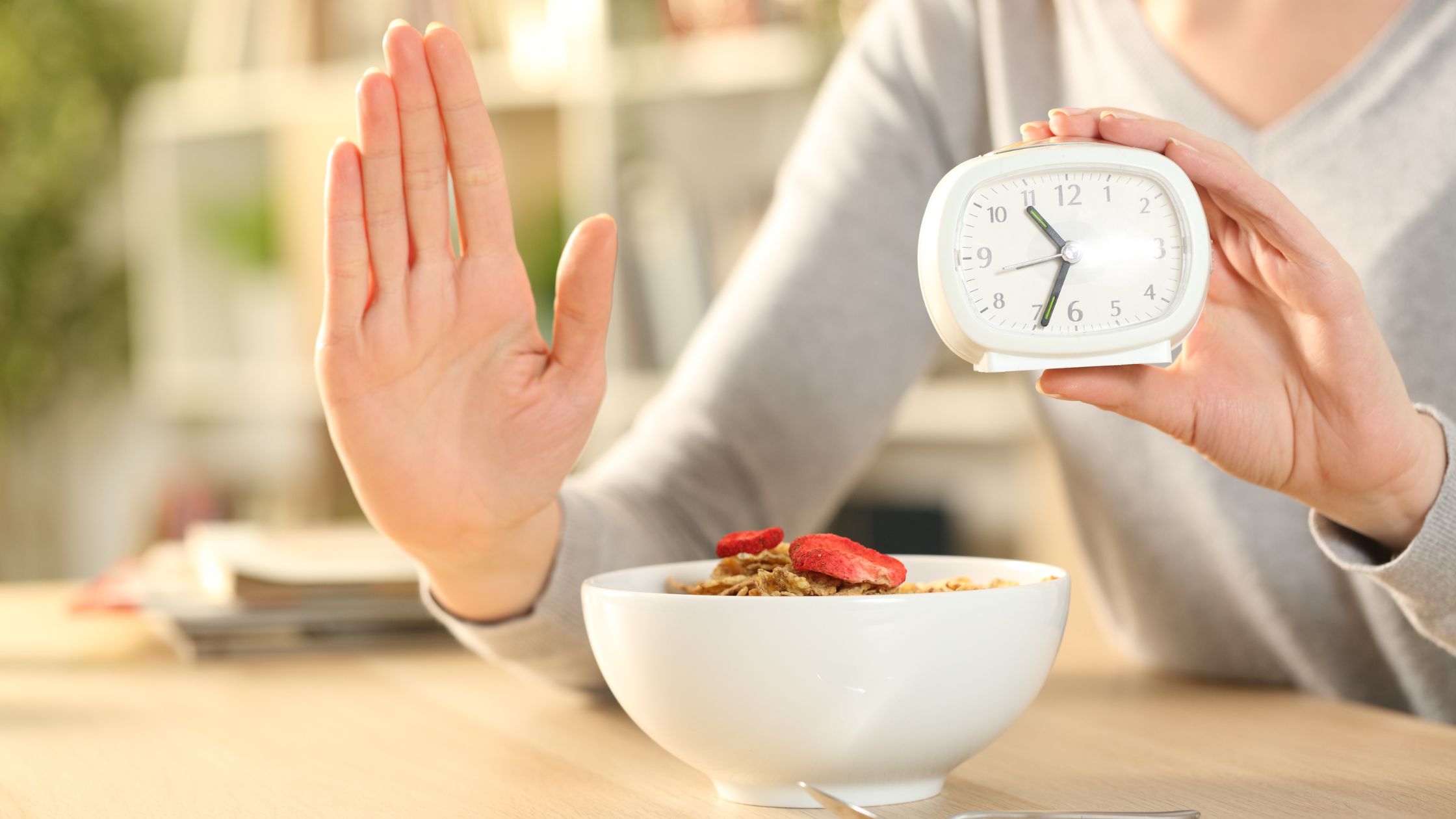 bowl of granola and fruit sits beside an analog timer and a hand held palm-forward to indicate "wait"