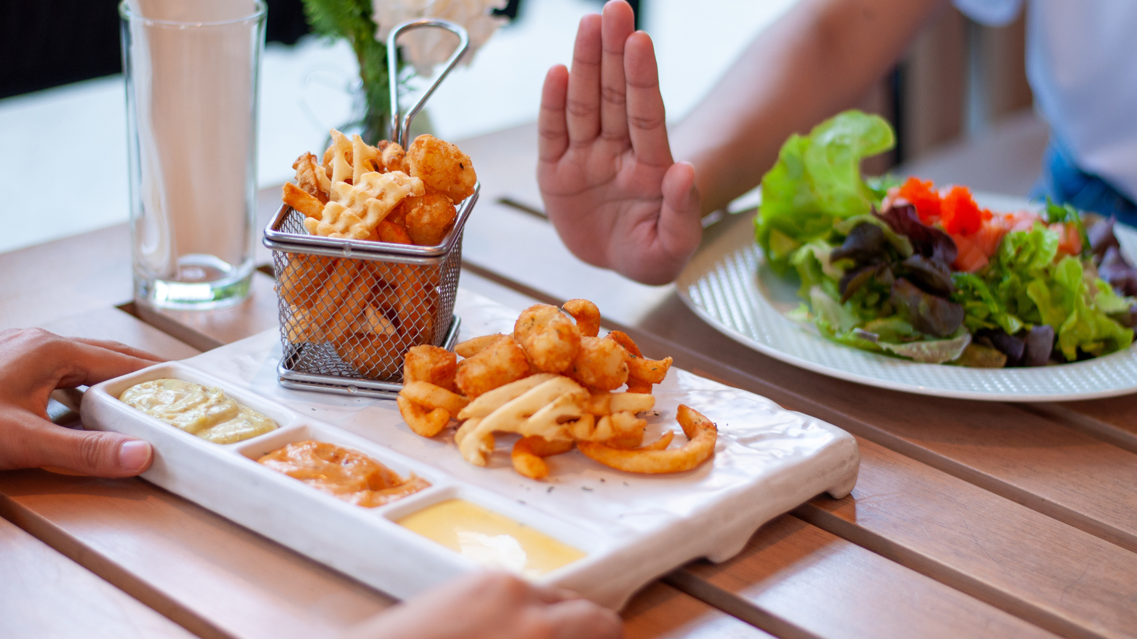 person eating a salad holds up a hand to refuse french fries