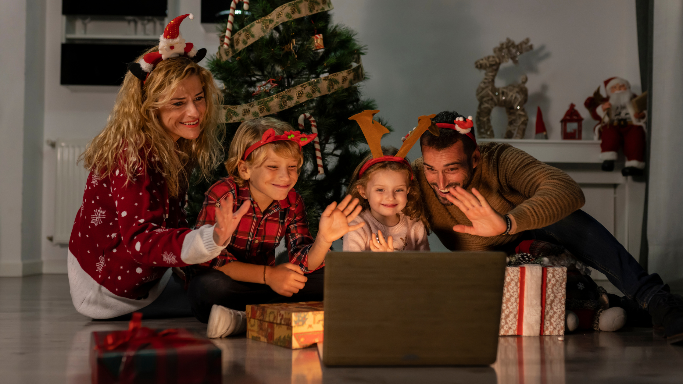 happy family of four smiles and waves at a computer screen video call