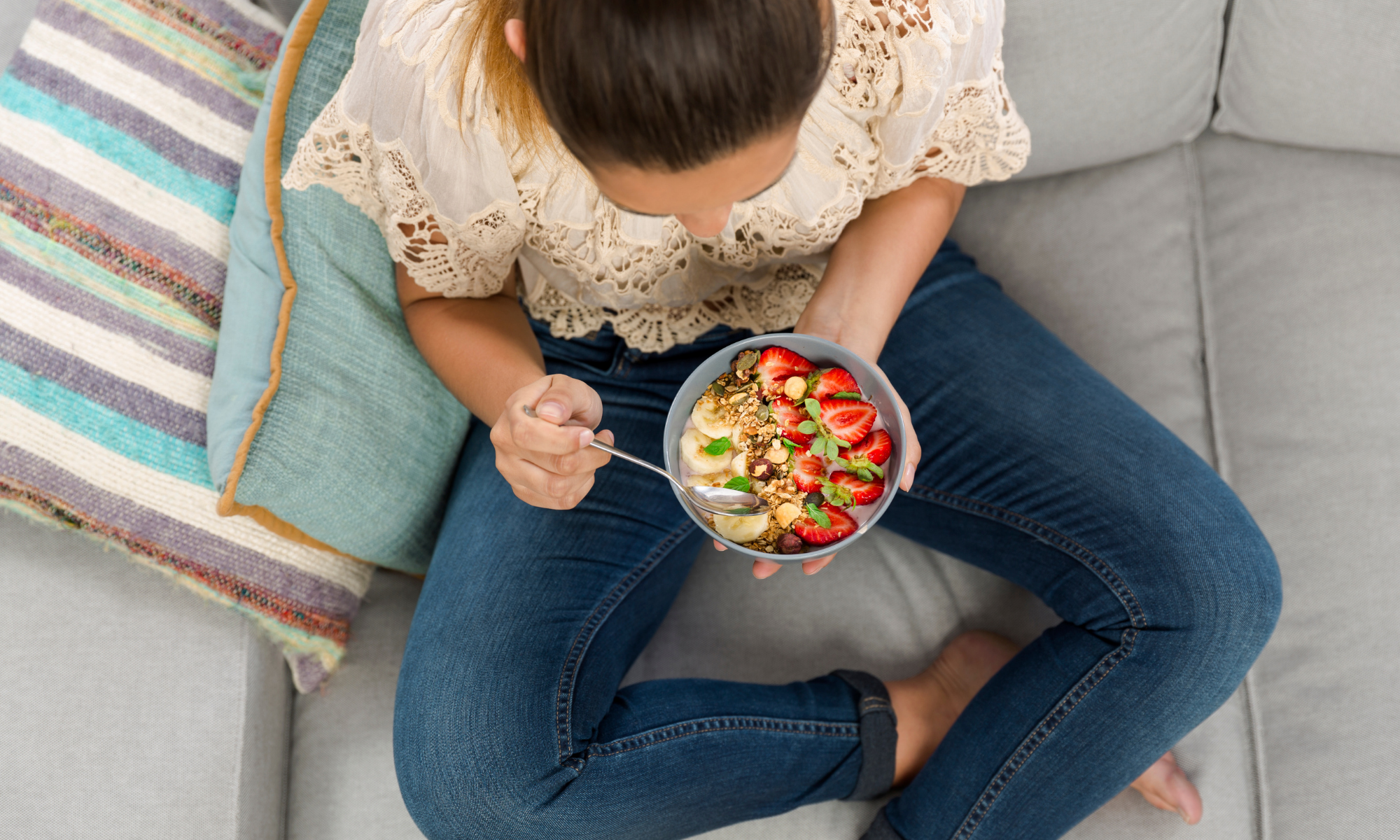 Woman on couch eating a bowl of various fruits and nuts