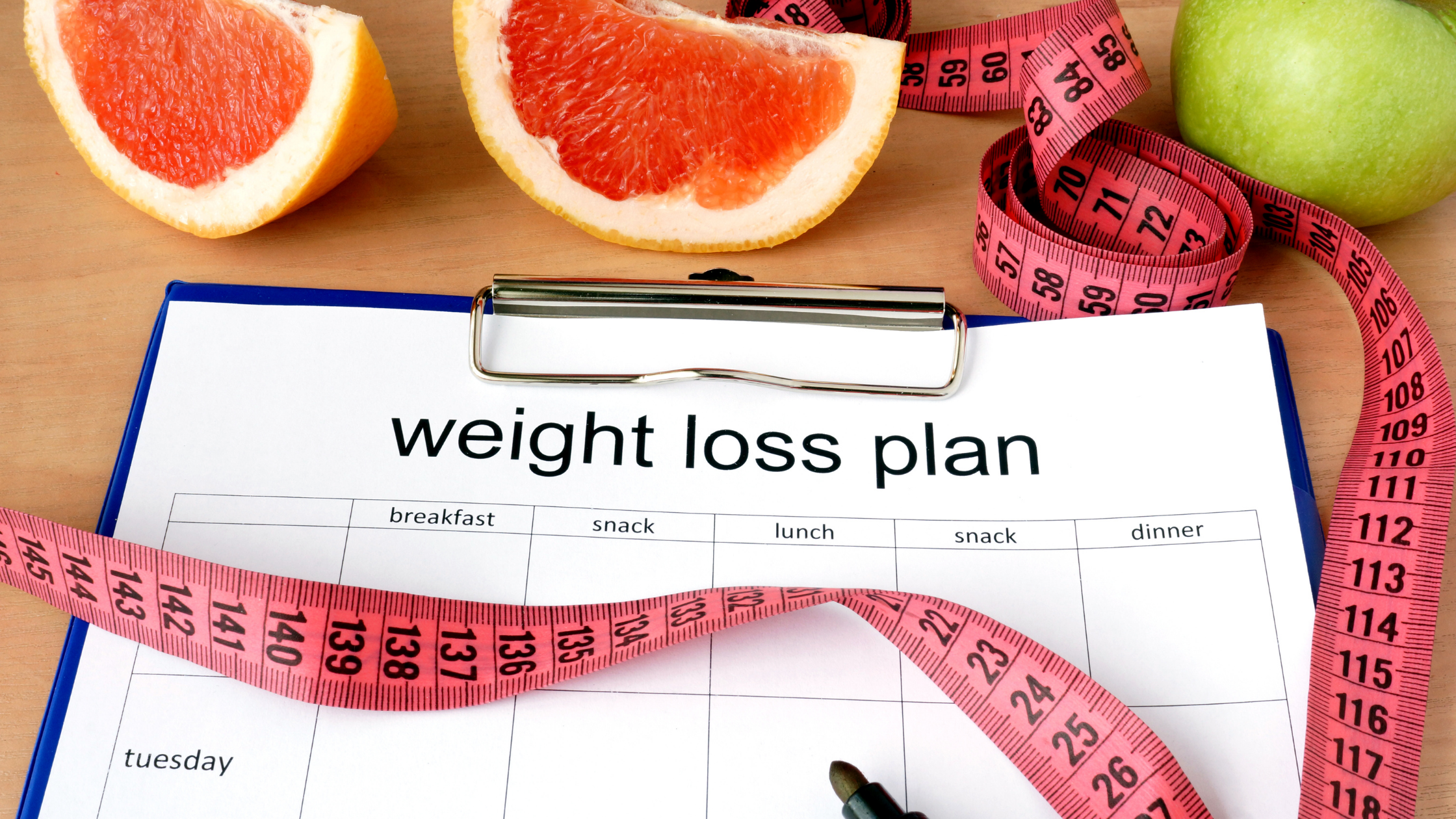 Clip-board labeled, "Weight Loss Plan", with a measuring tape and slice grapefruit beside it