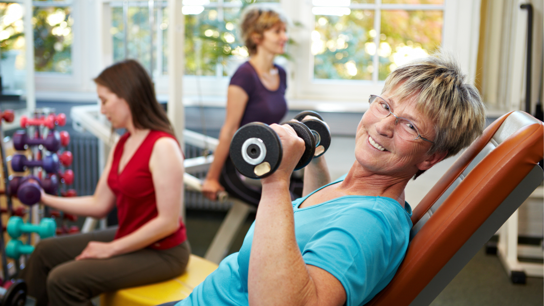 smiling senior woman raises a dumbbell at the gym