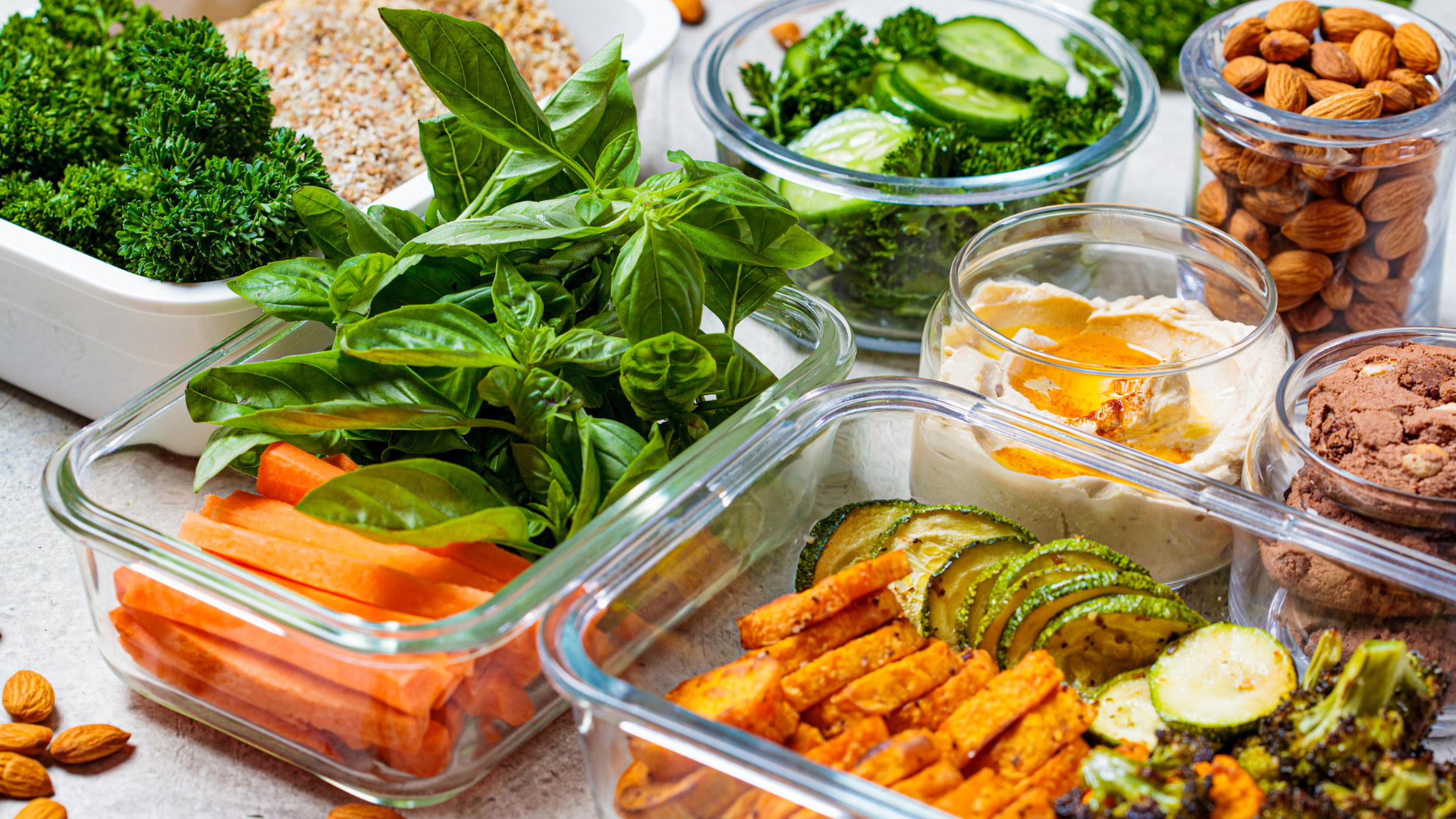 a variety of glass tupperware filled with cooked and raw vegetables and nuts