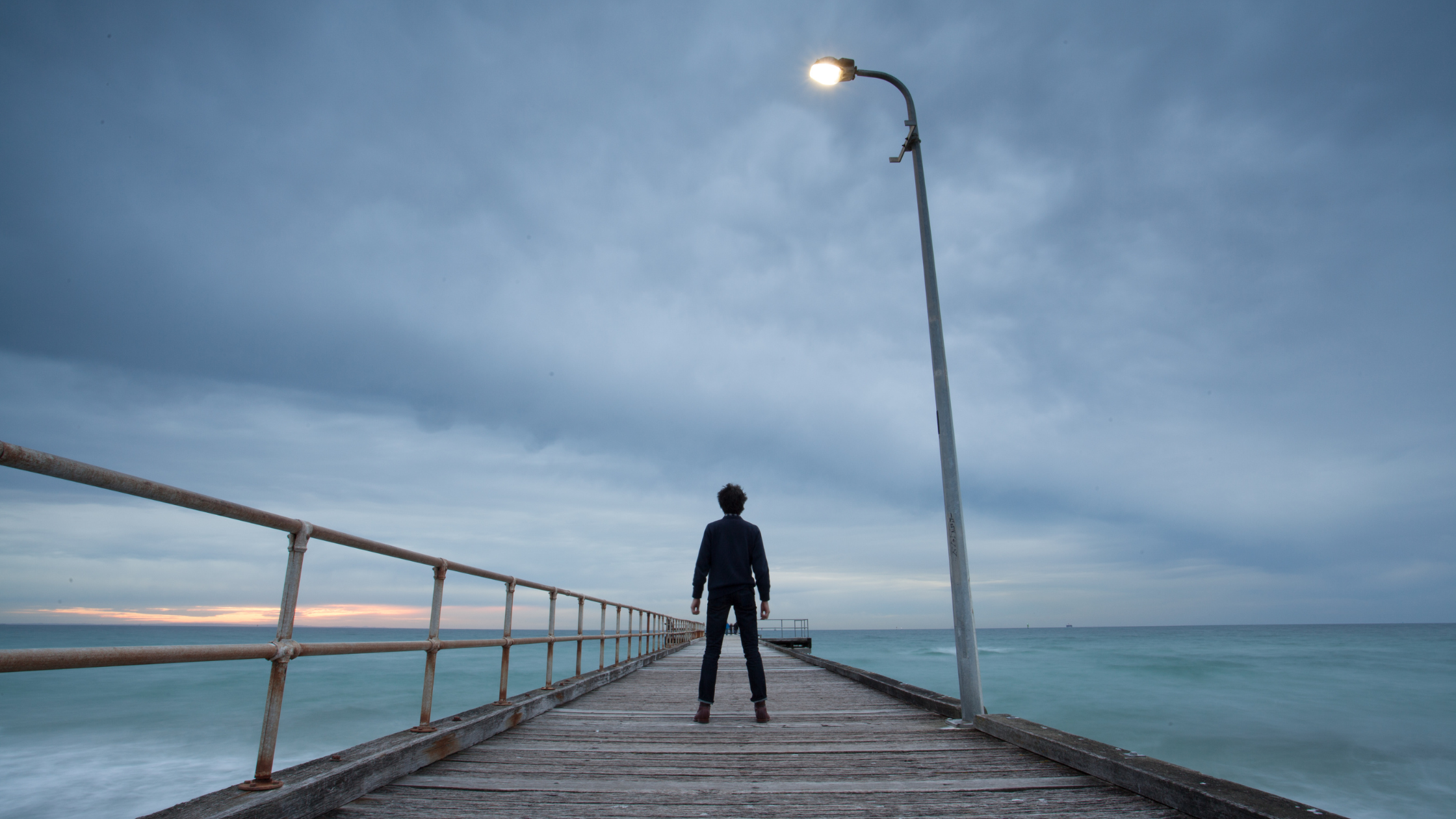 silhouette of a person standing alone on a cloudy pier