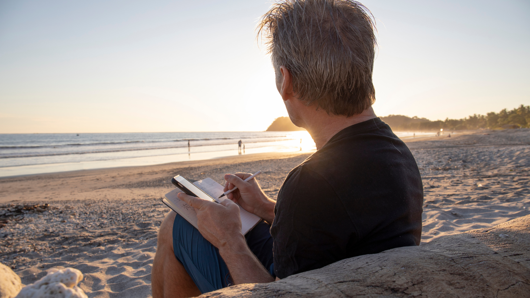 senior man sits on the beach writing in a notebook